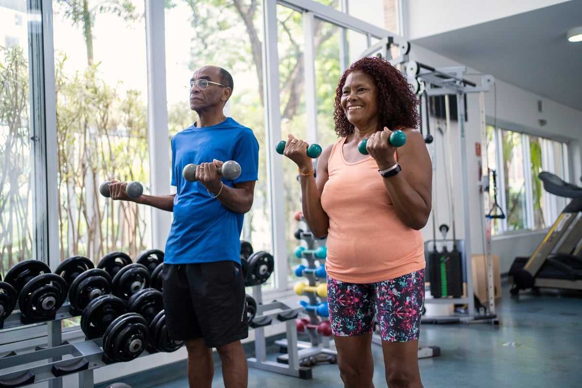 African American senior couple working out together with dumbbells in a gym, both smiling