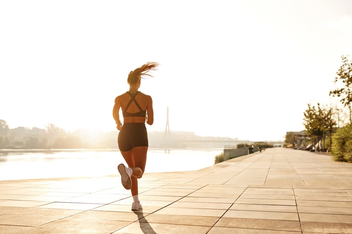 Active woman running along a waterfront path at sunset toward the light ahead